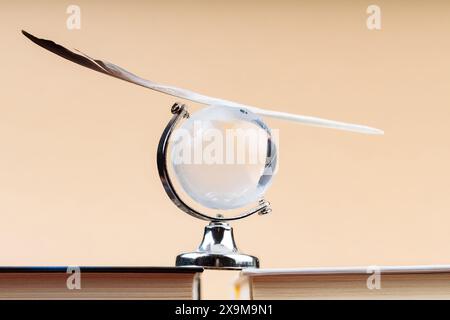 Glass Globe with Balancing Bird Feather on Stack of Books, Fragile Balance of Earth's Ecosystem Concept Stock Photo