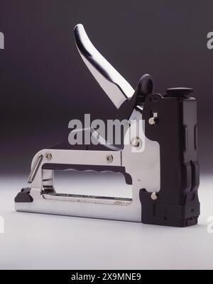 Heavy-duty manual staple gun on neutral background, metal construction with ergonomic handle, DIY upholstery carpentry tool Stock Photo