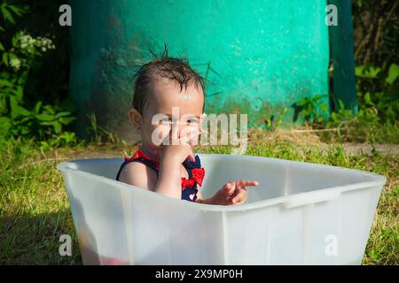 A baby in a plastic tub playing outdoors in the sunlight near a green tank, Belarus, Minsk Stock Photo