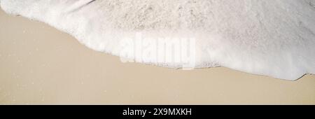 White fluffy foam from a wave breaking rolling onto the sandy beach background image Stock Photo