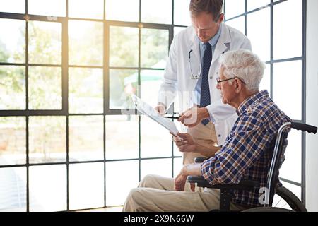 Doctor, man and wheelchair with document for reading, report or medical review in hospital. Medic, clipboard and person with disability in clinic for Stock Photo