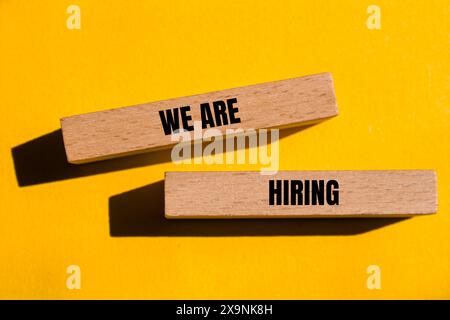 We are hiring words written on wooden blocks with yellow background. Conceptual we are hiring symbol. Copy space. Stock Photo