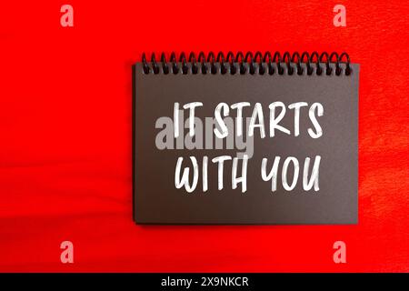 It starts with you message written on black notebook page with red background. Conceptual it starts with you symbol. Copy space. Stock Photo