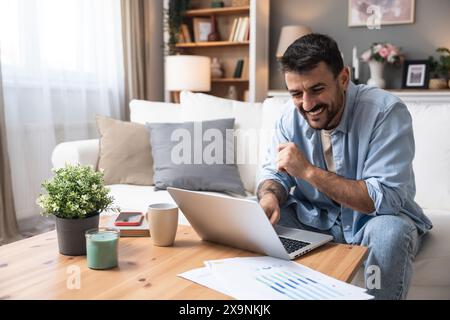 Young business man small startup company owner, working at home, checking the finances on graphs and laptop. Innovative young freelance male calculati Stock Photo