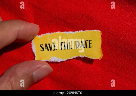 Save the date words written on ripped yellow paper with red background. Conceptual save the date symbol. Copy space. Stock Photo