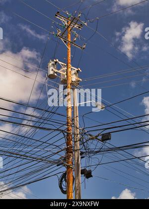 Tobago - Feb 2 2024: Many electrical cables connected to a wooden supply pole on the island of Tobago in the Caribbean. Shown against a blue sky with Stock Photo