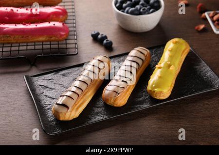 Different tasty glazed eclairs on wooden table, closeup Stock Photo