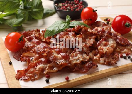 Slices of tasty fried bacon with different spices and tomatoes on wooden table, closeup Stock Photo