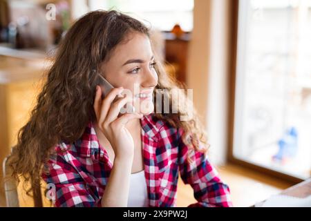 University student is writing her thesis on a laptop, sitting at home on the couch, making phone call. Stock Photo