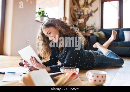 Female student lying on floor, reading books, studying for final exam at university. Beautiful student at home. Stock Photo
