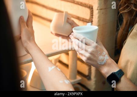 Unrecognizable craftswomen placing clay mugs into kiln Stock Photo