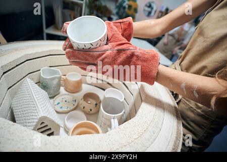 Unrecognizable female artisan taking glazed mug from kiln Stock Photo