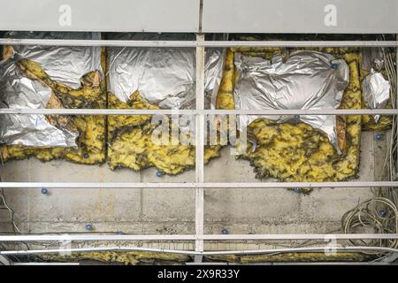 Demolished insulation with traces of fire on a concrete wall behind an opened facade cover on a building, concept for construction engineering and the Stock Photo