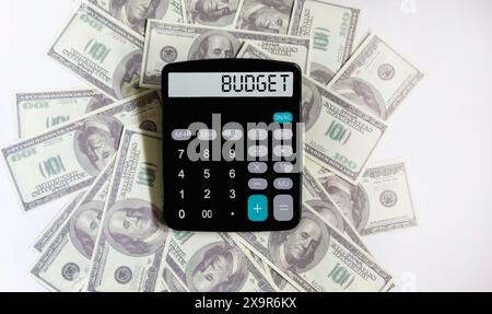 Calculator with the word BUDGET on the display. One hundred dollar bills lie on a white background. Conceptual photo. Stock Photo