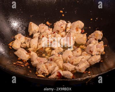 Tender chicken sizzles in a cast iron wok alongside fiery red chilies and glistening garlic, promising a spicy culinary adventure. Stock Photo