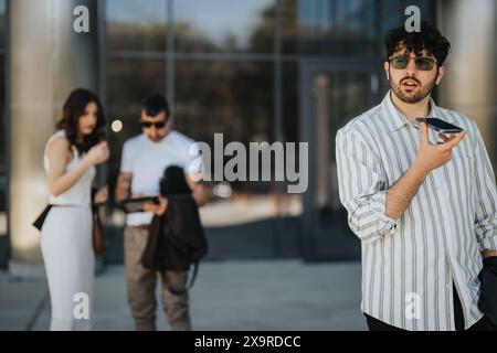 Young man using voice command on smart phone in urban setting with blurred couple in background Stock Photo