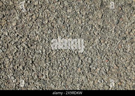 Grey road backdrop. Asphalt surface, covered with stones on the resin base. Detailed texture and background of the road close-up. Uneven surface Stock Photo