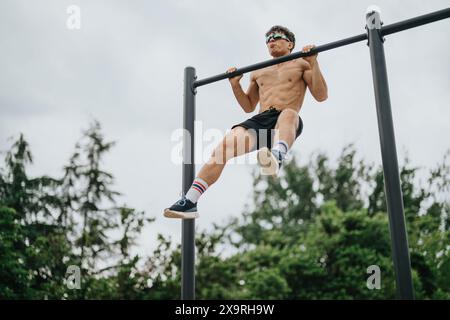 Young man doing pull-ups on metal bars in outdoor park Stock Photo