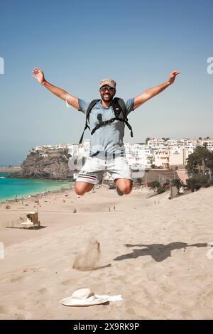 italian mediterranean man posing happy while jumping on Morro Jable beach in Fuerteventura Stock Photo