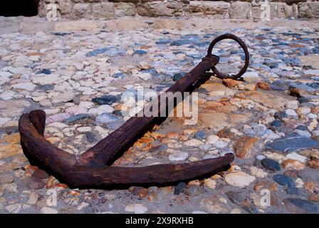 Old rusty anchor on sea rocks filmed in a fortress in Heraklion, Crete, Greece Stock Photo