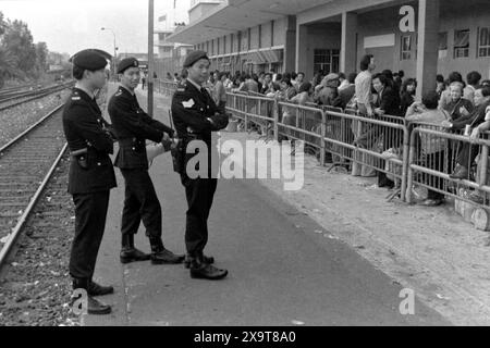 Passengers waiting for a southbound diesel train, Lo Wu Railway Station, Kowloon-Canton Railway, Hong Kong, Lunar New Year 1981. The waiting crowd have all just returned to Hong Kong from mainland China.  Policemen on the platform are engaged in crowd management, due to high holiday-season numbers of passengers. This was before the KCR was electrified in the early 1980s, and the stations and facilities upgraded. Stock Photo