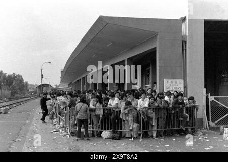 Passengers waiting for a southbound diesel train, Lo Wu Railway Station, Kowloon-Canton Railway, Hong Kong, Lunar New Year 1981. The waiting crowd have all just returned to Hong Kong from mainland China.  Policemen on the platform are engaged in crowd management, due to high holiday-season numbers of passengers. This was before the KCR was electrified in the early 1980s, and the stations and facilities upgraded. Stock Photo