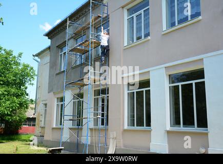 A painter climbs a ladder onto scaffolding to paint the wall of a house. Stock Photo