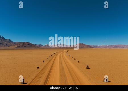 A remote road winds through the vast Namib Naukluft desert, with majestic mountains rising on the horizon Stock Photo