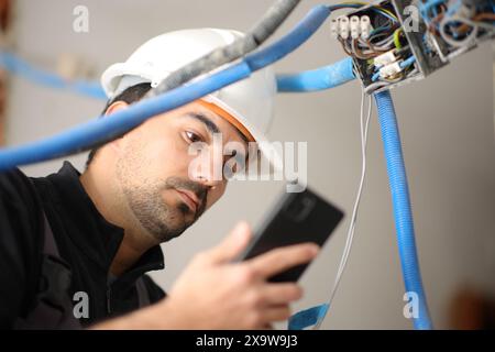 Electrician checking information on phone installing electrical system in a house under renovation Stock Photo