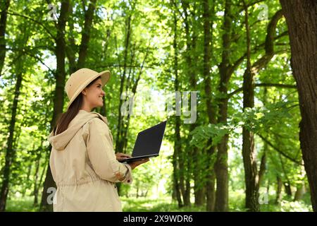 Forester with laptop examining plants in forest, space for text Stock Photo