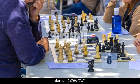 A man is playing chess with another man. The man in the blue shirt is looking at the board Stock Photo
