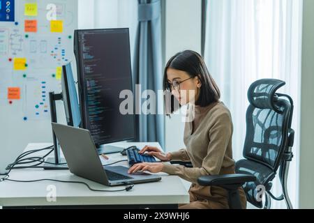 Asian prompt engineer develop coding app with software data sitting in front of computer monitor at office Stock Photo