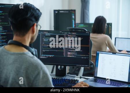 Asian software developers working on multiple screens displaying code and application diagrams in a modern office Stock Photo