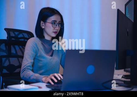 Asian woman  software development working on coding  computer screen and flowchart at night in modern office Stock Photo