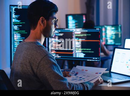 Asian software developers working on multiple screens displaying code and application diagrams at night in modern office Stock Photo