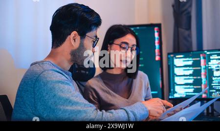 Asian software developers teams working on multiple screens displaying code and application diagrams at night in modern office Stock Photo
