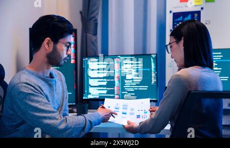 Asian software developers teams working on multiple screens displaying code and application diagrams at night in modern office Stock Photo