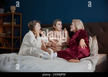 Happy senior female friends with cotton mask on face having nice conversation Stock Photo