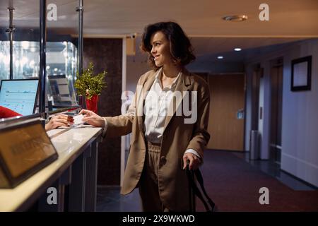 Young elegant businesswoman at hotel reception taking key from room Stock Photo