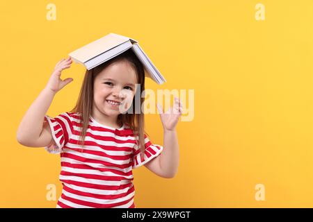 Cute little girl with open book on orange background. Space for text Stock Photo