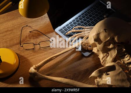 Waiting concept. Human skeleton sleeping at wooden table with laptop Stock Photo