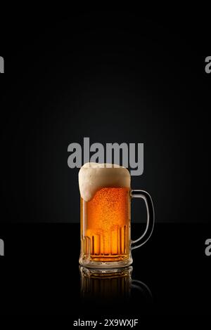 Glass mug of cold, refreshing, golden beer, topped with thick foam against black studio background. Stock Photo