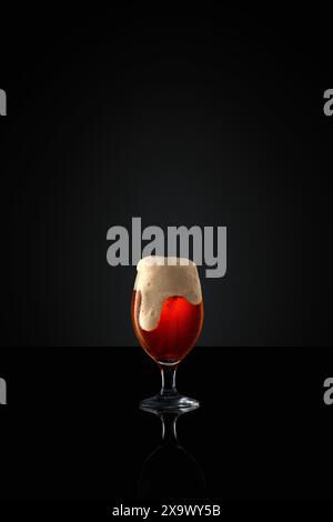 Glass goblet brimming with craft, dark beer, topped with thick, creamy foam against black studio background. Stock Photo