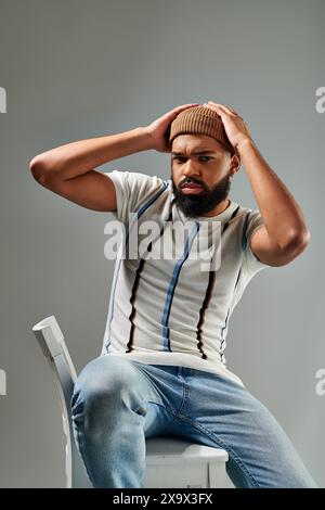 An African American man in stylish clothing sitting on top of a white chair, contemplating with a thoughtful expression. Stock Photo