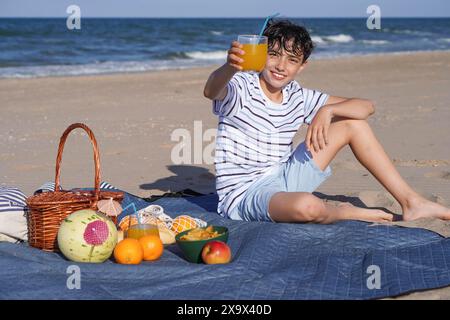 preteen boy picnicking healthy food and drink on the beach  happily with a glass of orange juice. summer concept Stock Photo