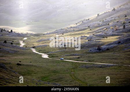 Car on a Gravel road to traditional Lukomir village, passing Bjelasnica plateau, surrounded with spectacular landscape, Bosnia and Hercegovina Stock Photo