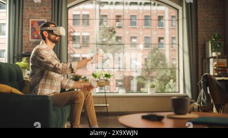 Adult Bearded Male Using Virtual Reality Headset and Controllers at Home. Creative Man Sitting on a Sofa in Living Room, Playing VR Video Game or Working with Special Digital Tools. Stock Photo