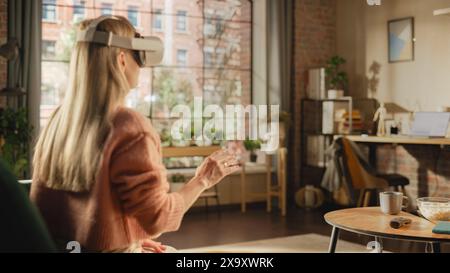 Over the Shoulder Footage of a Female Freelancer Using Virtual Reality Headset and Controllers for Her Project while Sitting on a Couch. Young Woman Working in Futuristic Metaverse App. Stock Photo