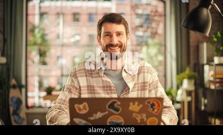 Handsome Bearded Young Adult Man Having an Online Conversation on a Laptop Computer in Creative Office Environment. Happy Specialist Browsing Internet and Social Media Platforms. Stock Photo