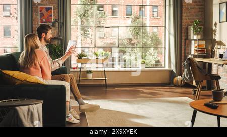 Man and Woman Using Tablet While Sitting on a Couch in a Stylish Apartment. A Young Couple Calling Family and Friends Online Through Video Chat Using Technology Stock Photo